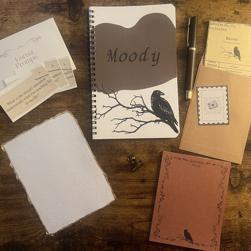 Writer's Corner — Autumn 2026, flat lay featuring the Moody raven notebook, journal prompts, pen, archive card, gold-edged deckled paper, and story insert.